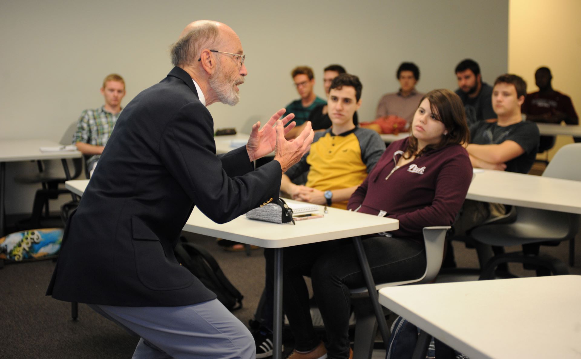 Professor in a suit gesturing passionately during a lecture in a classroom filled with attentive students